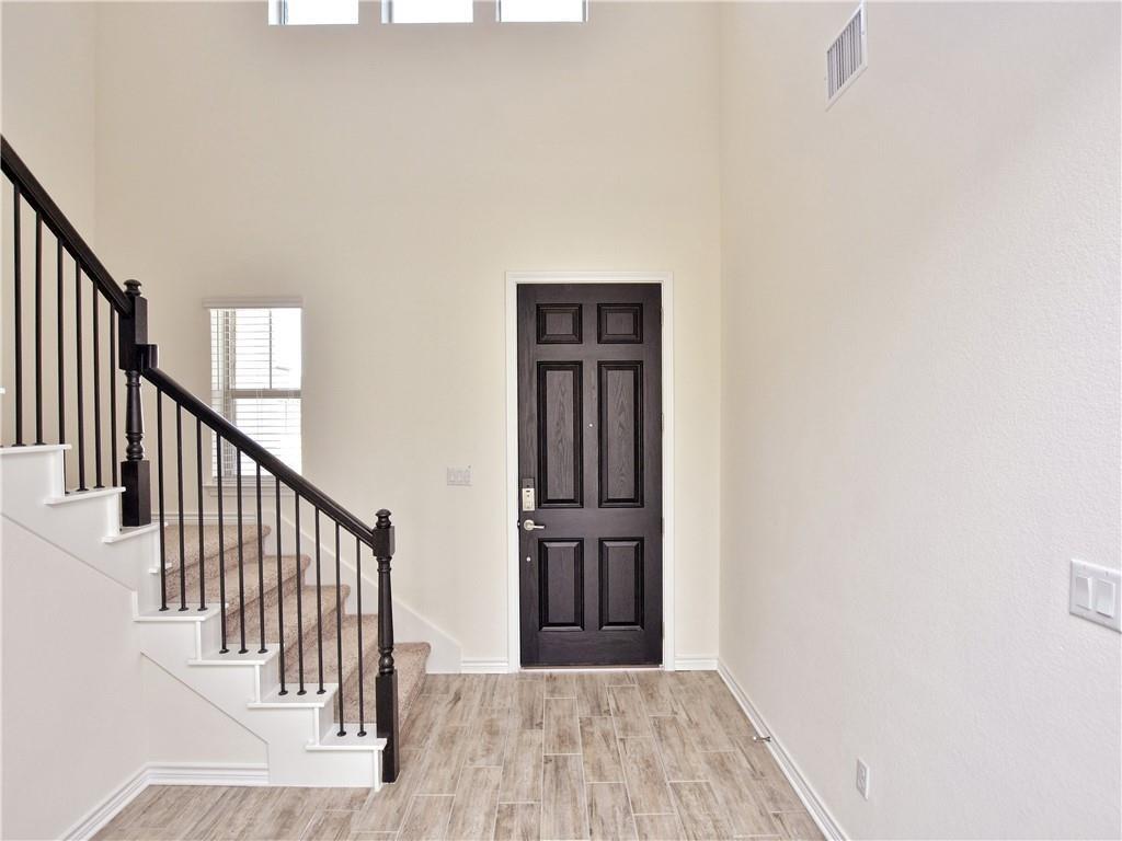 1836 Turtle Bay Loop Leander, TX 78641 - Photo 3 of 32 Two-story foyer featuring wood-finish flooring, a paneled entry door, and a staircase with black iron balusters and carpeted treads