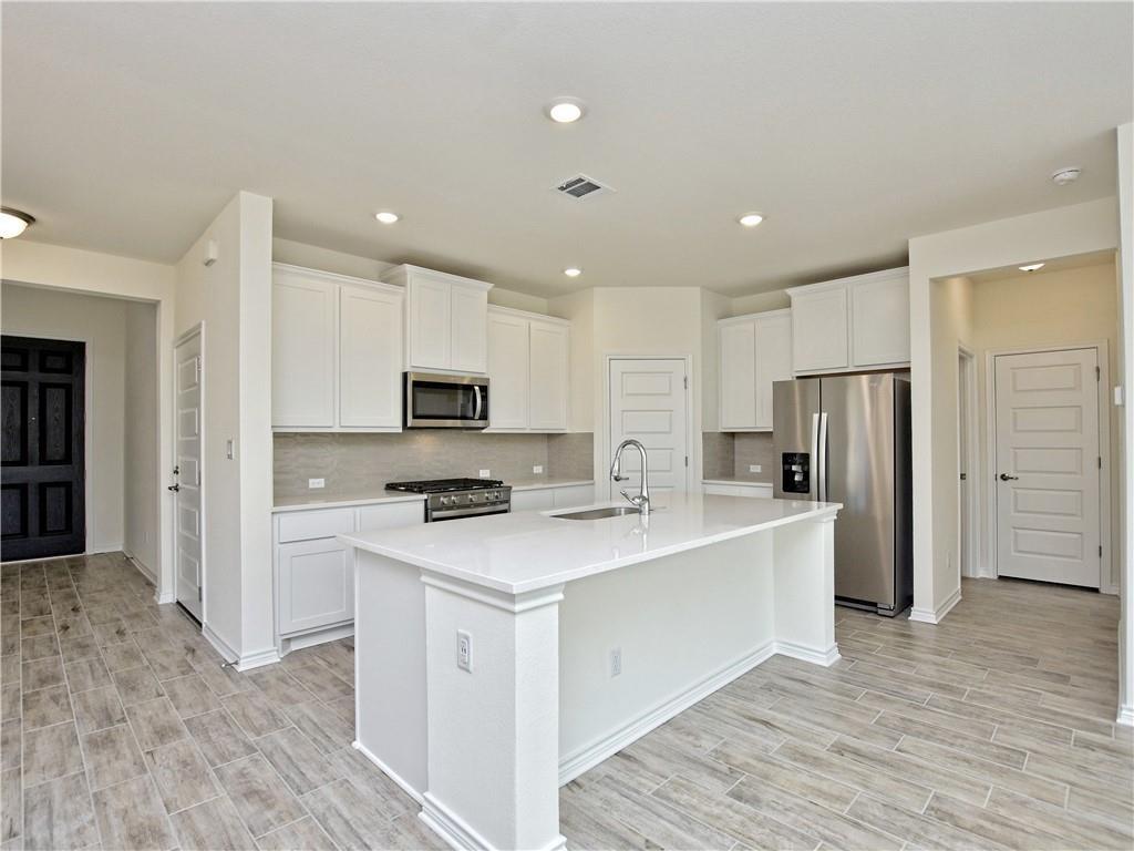 1836 Turtle Bay Loop Leander, TX 78641 - Photo 4 of 32 Modern kitchen featuring a large central island with an integrated sink, white cabinetry, stainless steel appliances, and wood-finish tile flooring