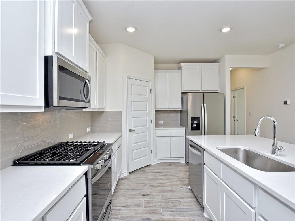 1836 Turtle Bay Loop Leander, TX 78641 - Photo 6 of 32 Modern kitchen featuring white shaker cabinetry, stainless steel appliances, light countertops, a tile backsplash, and wood-finish flooring