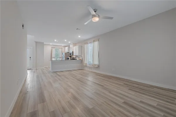 a view of an empty room with wooden floor and a ceiling fan