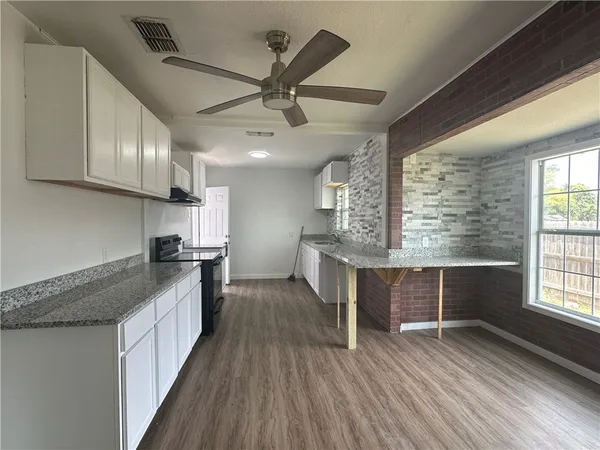 a kitchen with granite countertop a stove a sink and white cabinets with wooden floor
