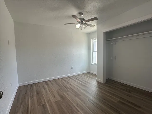 a view of an empty room with wooden floor and a fan