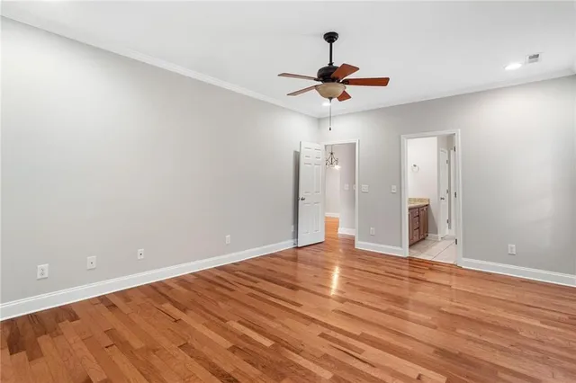 a view of an empty room with wooden floor and a ceiling fan