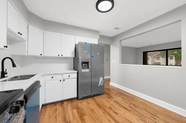 a kitchen with granite countertop a refrigerator a stove a sink dishwasher and white cabinets with wooden floor