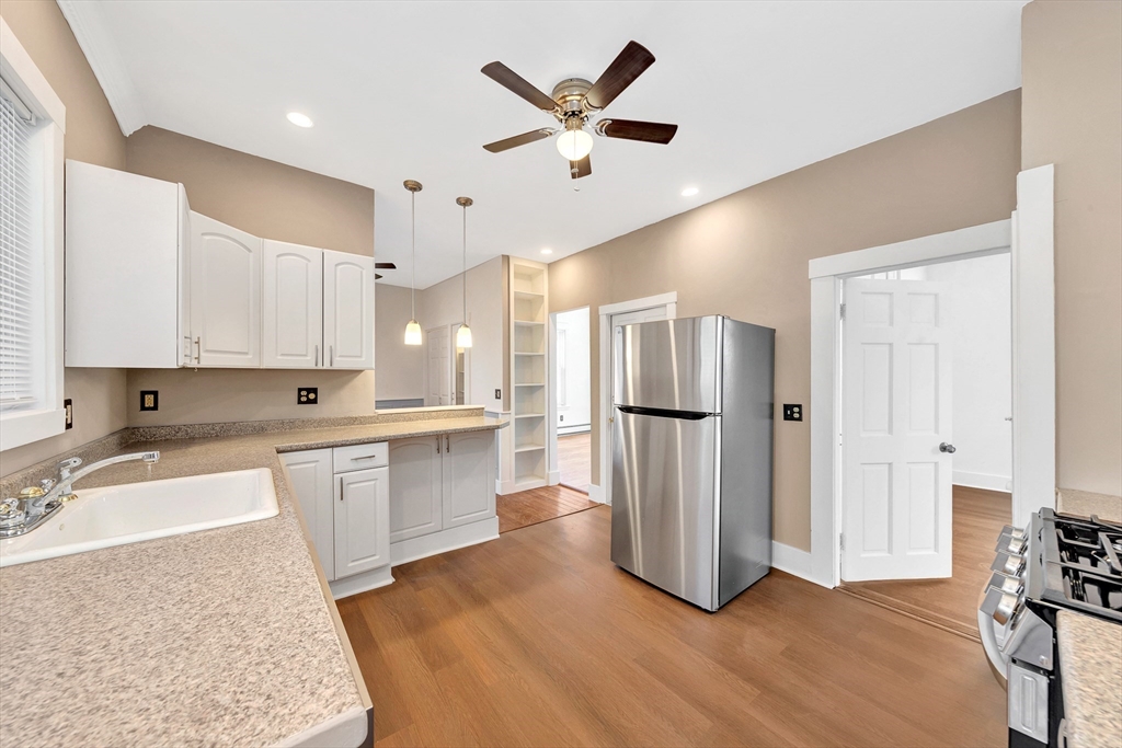 24 Taylor Street, Unit 1 Gloucester, MA 01930 - Photo 15 of 29 a large white kitchen with a refrigerator a sink dishwasher a stove and a dining table with wooden floor