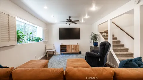 a living room with furniture a ceiling fan a flat screen tv and a large window