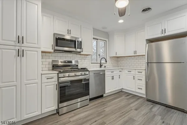 a kitchen with white cabinets stainless steel appliances and wooden floor