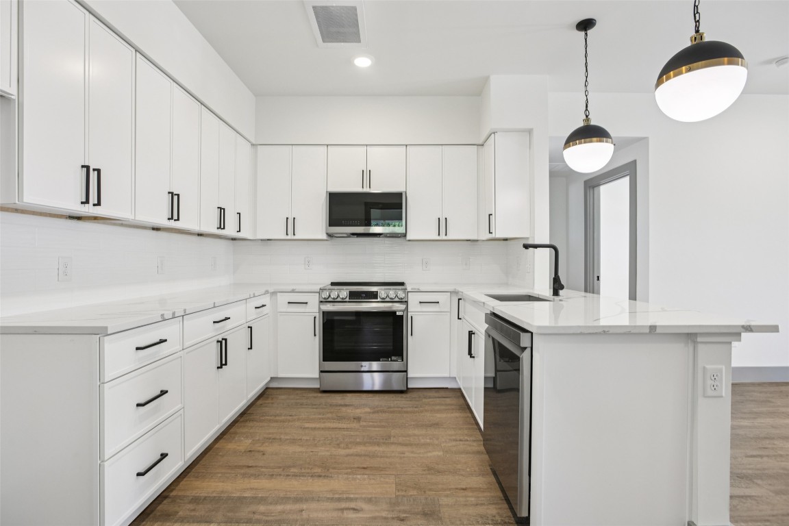 2450 Wickersham Lane, Unit 1917 Austin, TX 78741 - Photo 3 of 18 Kitchen featuring backsplash, dark wood finished floors, appliances with stainless steel finishes, a peninsula, and white cabinets