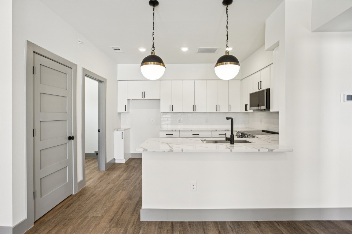 2450 Wickersham Lane, Unit 1917 Austin, TX 78741 - Photo 5 of 18 Kitchen featuring light stone counters, backsplash, decorative light fixtures, white cabinets, and dark wood-style flooring