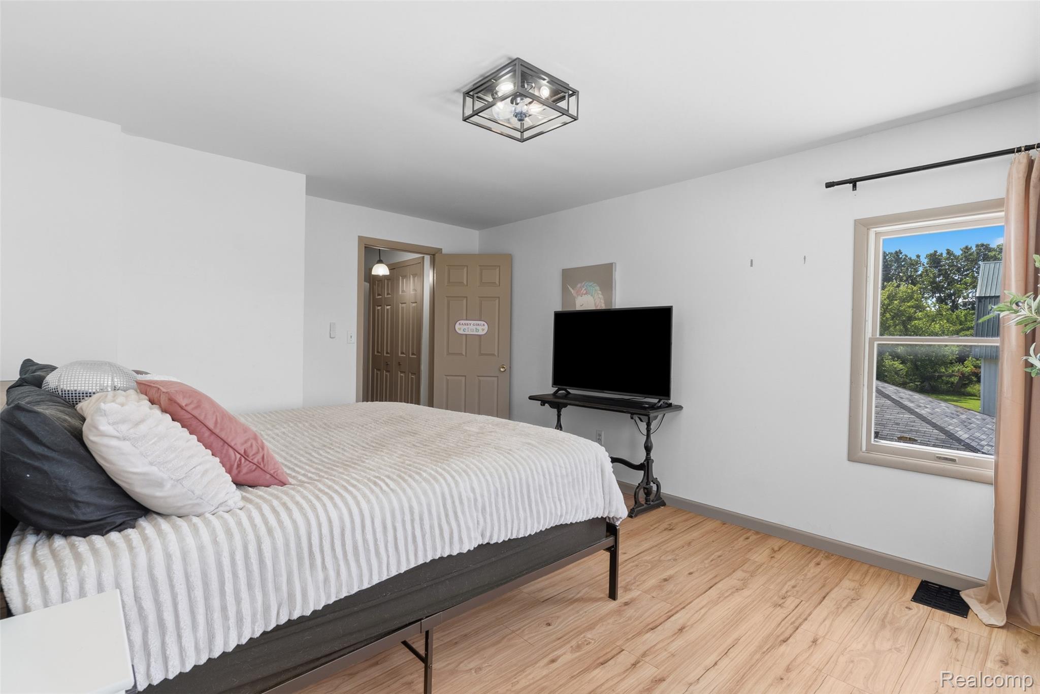 5843 West Dewey Road Owosso, MI 48867 - Photo 34 of 58 Bright bedroom featuring a large window, wood-finish flooring, a contemporary ceiling light fixture, and a paneled door