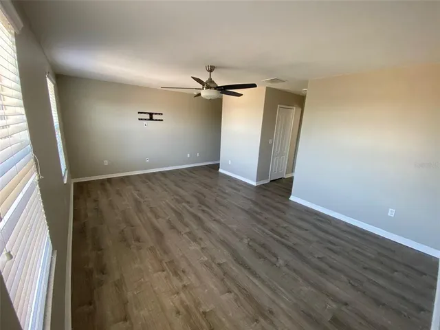 an empty room with wooden floor ceiling fan and windows