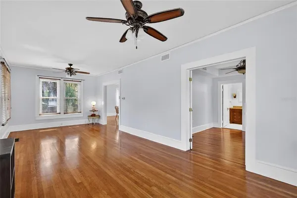 an empty room with wooden floor chandelier fan and windows