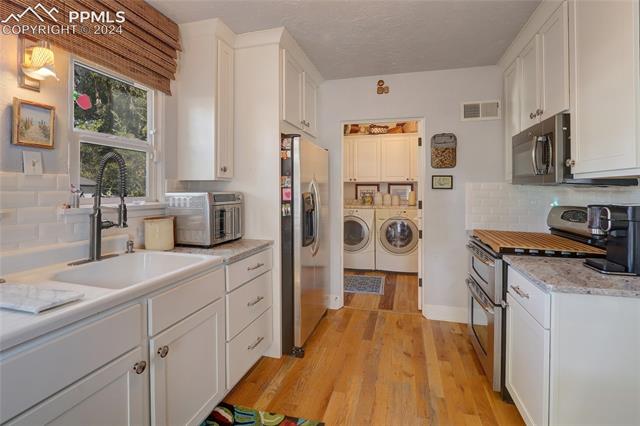 314 West Cheyenne Road Colorado Springs, CO 80906 - Photo 14 of 36 Kitchen with light hardwood / wood-style floors, white cabinetry, independent washer and dryer, tasteful backsplash, and stainless steel appliances