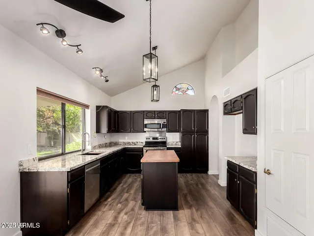 a kitchen with granite countertop a refrigerator a sink dishwasher a stove and white cabinets with wooden floor