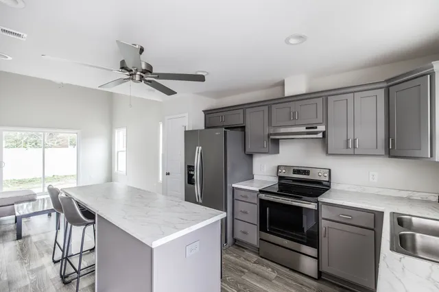 a kitchen with stainless steel appliances a stove a sink dishwasher a refrigerator with a dining table and chair