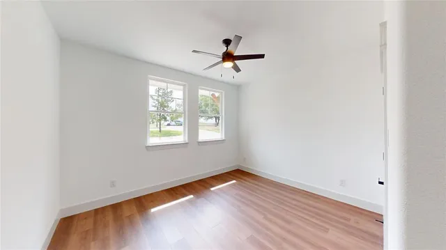 an empty room with wooden floor ceiling fan and windows