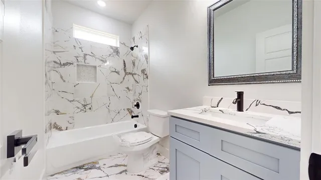 a bathroom with a granite countertop bathtub sink vanity mirror and toilet