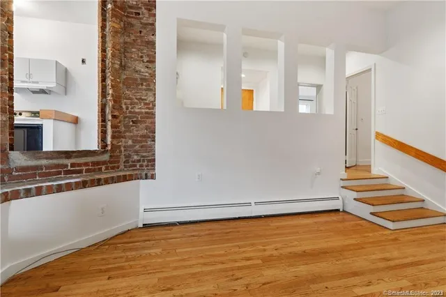 a view of an empty room with wooden floor and a kitchen