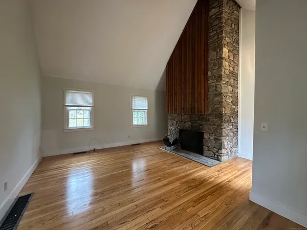 an empty room with wooden floor fireplace and windows