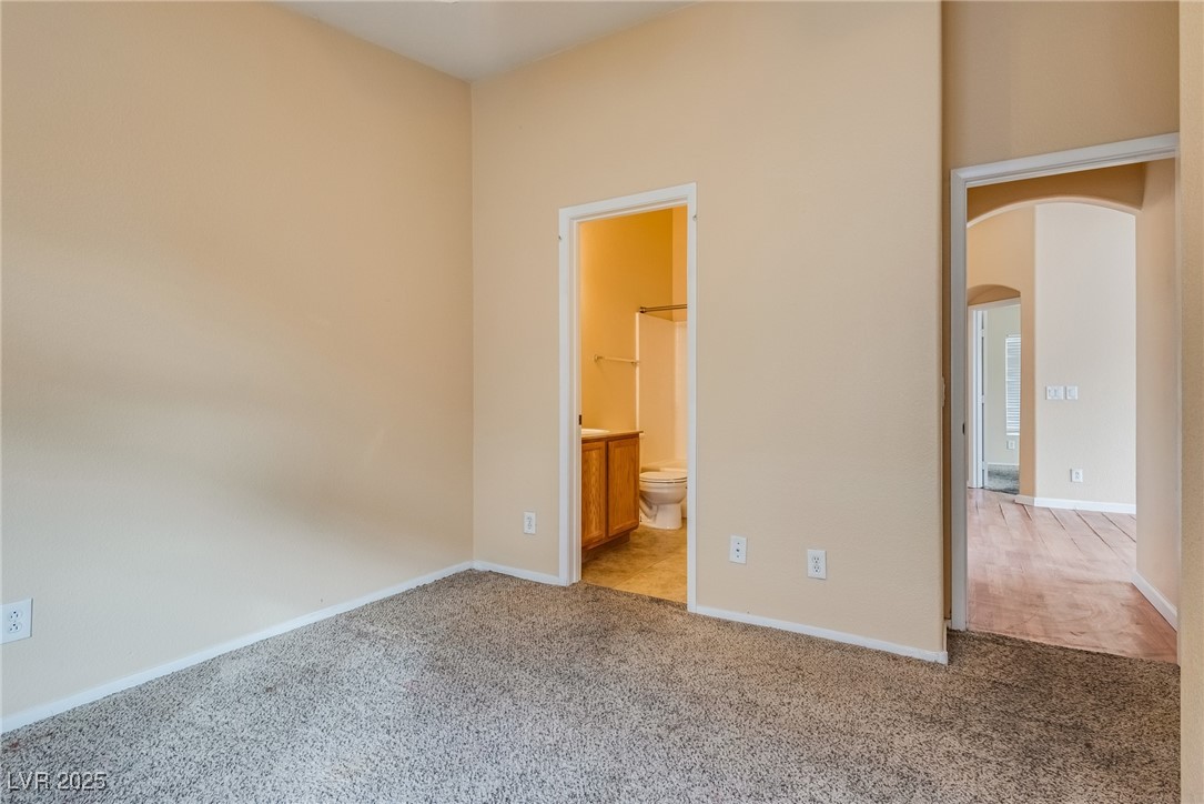 6354 Rusticated Stone Avenue, Unit 101 Henderson, NV 89011 - Photo 17 of 21 Unfurnished bedroom with arched walkways, light carpet, and ensuite bathroom