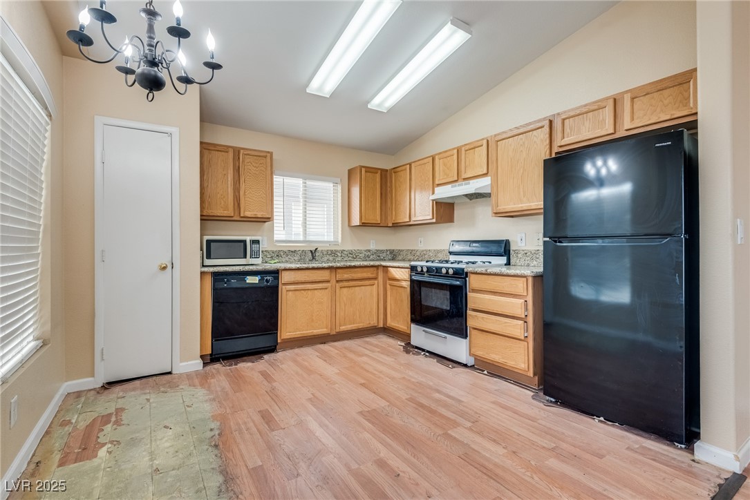6354 Rusticated Stone Avenue, Unit 101 Henderson, NV 89011 - Photo 6 of 21 Kitchen with black appliances, a chandelier, vaulted ceiling, light wood-type flooring, and under cabinet range hood