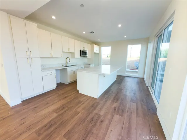 a living room with stainless steel appliances granite countertop a refrigerator a sink dishwasher and a stove with wooden floor