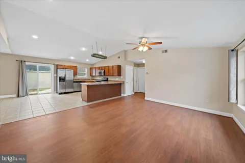 an empty room with wooden floor kitchen view and a window