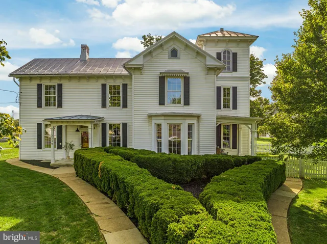 a view of a brick house next to a big yard and large trees