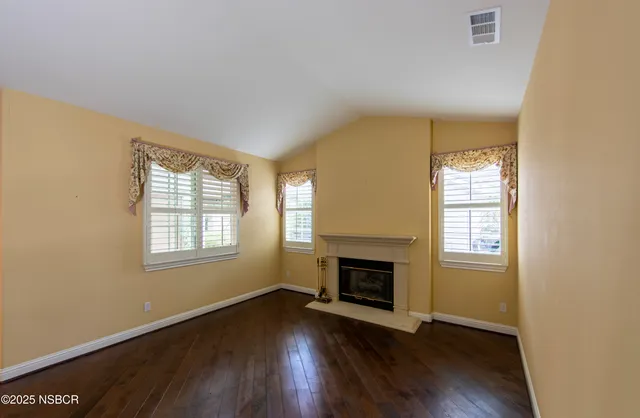 an empty room with wooden floor fireplace and windows