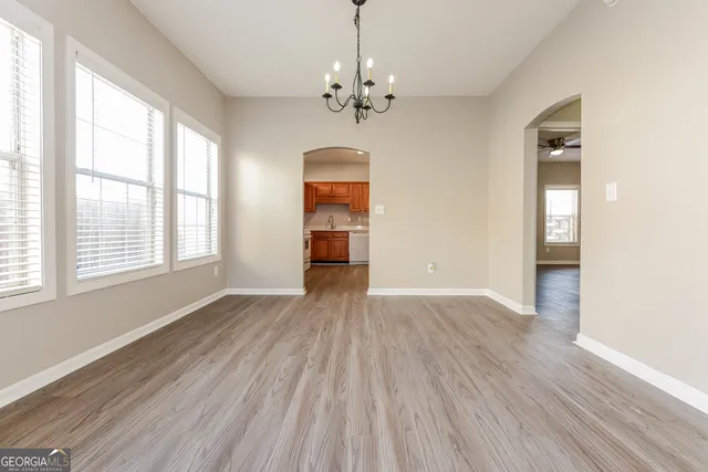 an empty room with wooden floor chandelier and windows