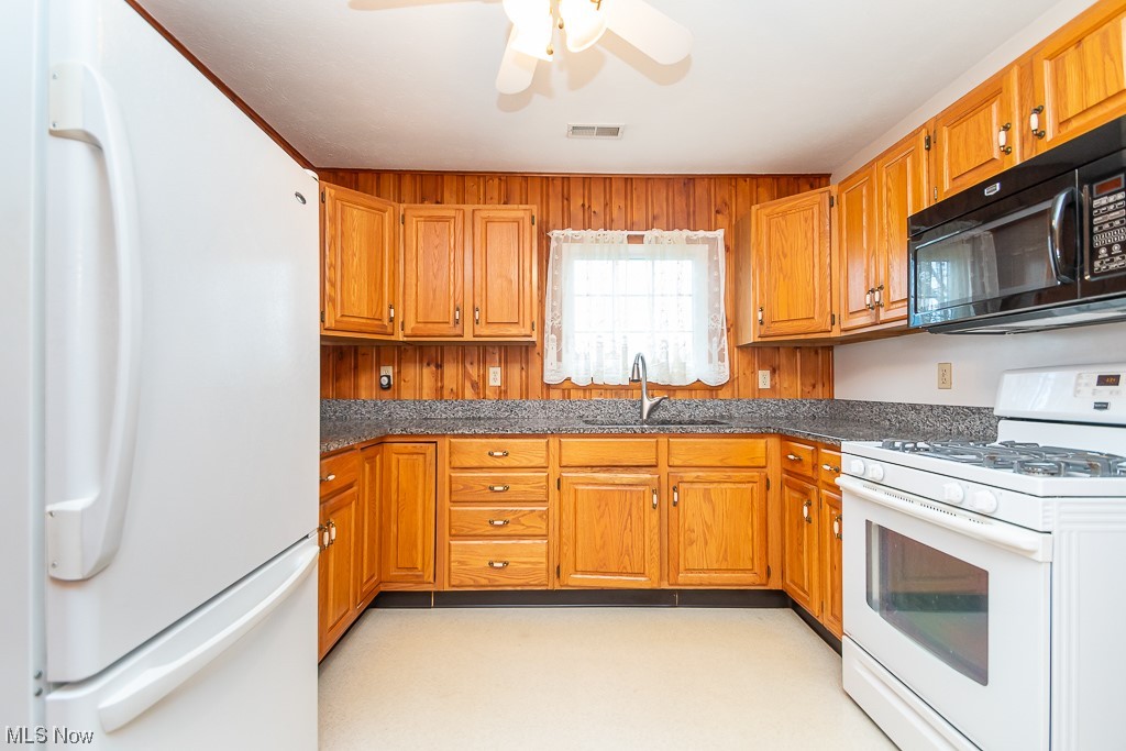 5 Pleasantview Vermilion, OH 44089 - Photo 7 of 37 Kitchen with sink, white appliances, ceiling fan, and dark stone countertops