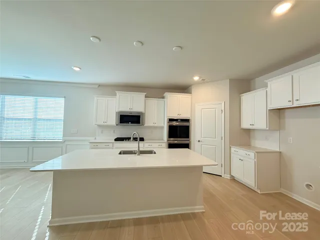 a large white kitchen with kitchen island a sink stainless steel appliances and cabinets