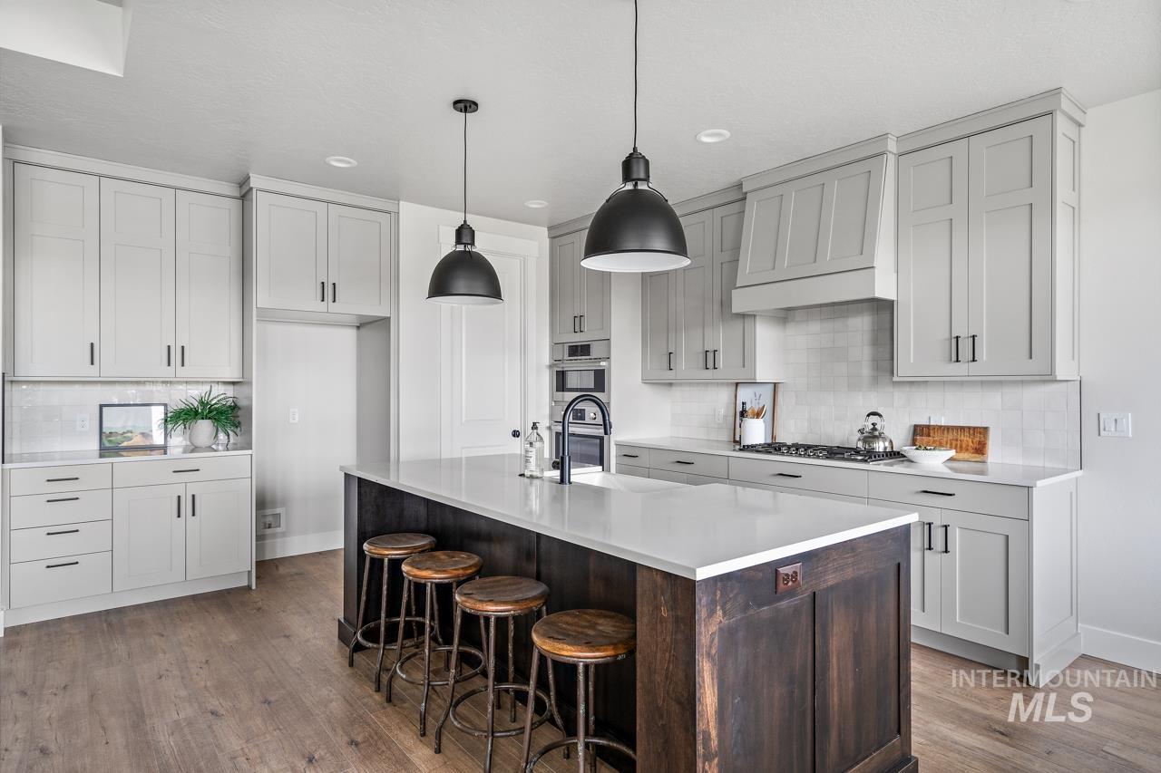 1101 East Crescendo Street Meridian, ID 83642 - Photo 13 of 31 Kitchen with decorative backsplash, custom range hood, a kitchen bar, dark brown cabinets, and an island with sink