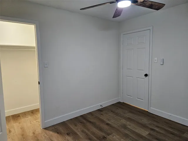 a view of an empty room with wooden floor fan and window