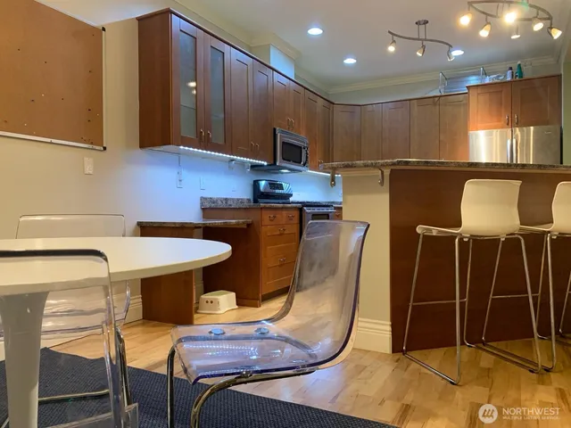 a kitchen with stainless steel appliances wooden floor dining table chairs cabinets and a sink