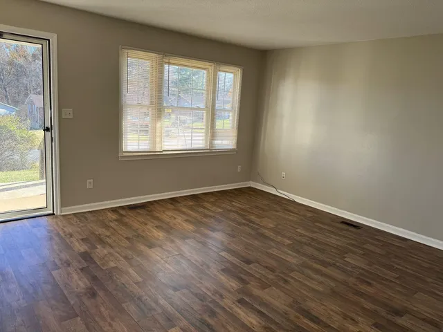 a view of an empty room with wooden floor and a window