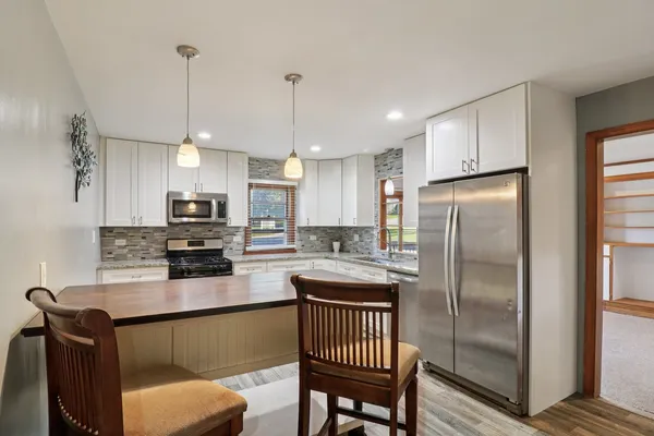 a kitchen with stainless steel appliances granite countertop a refrigerator a sink a stove a dining table and chairs