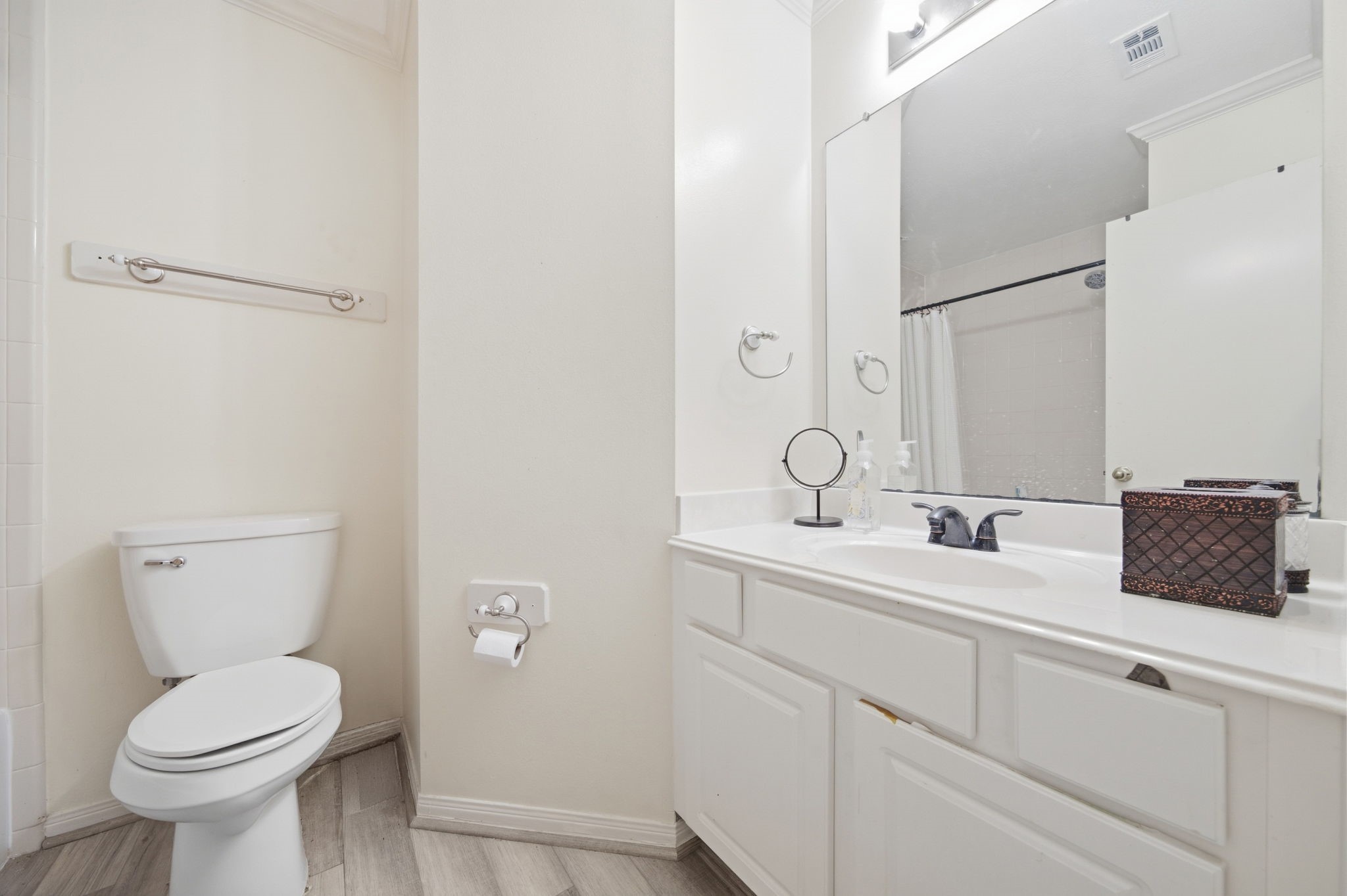 6911 River Road Richmond, TX 77469 - Photo 29 of 36 Wood-look herringbone flooring and a crisp white vanity define this secondary full bathroom, offering solid everyday functionality. A wide frameless mirror reflects the space, while the adjacent tub and shower combination provides classic utility for guests.