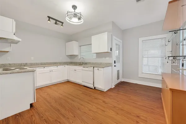 a kitchen with stainless steel appliances granite countertop a stove a sink dishwasher and white cabinets with wooden floor