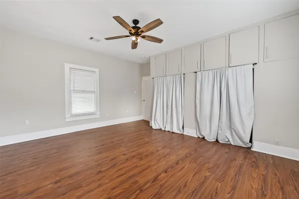 an empty room with wooden floor chandelier fan and windows