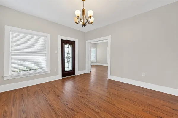 an empty room with wooden floor chandelier and windows