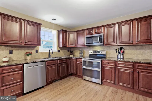 a kitchen with stainless steel appliances granite countertop wooden cabinets a stove top oven a sink and dishwasher with wooden floor