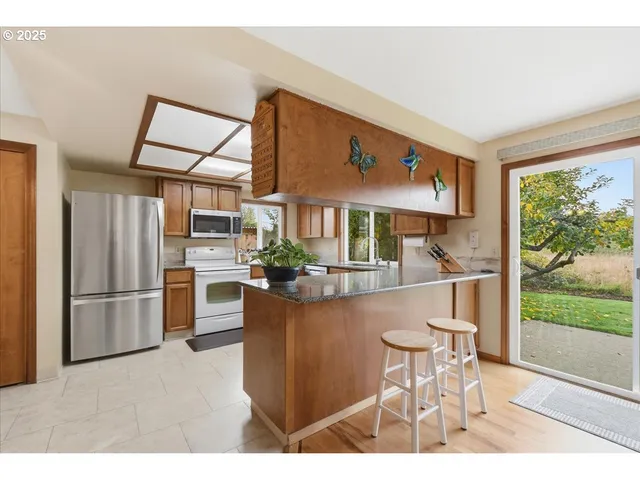 a kitchen with stainless steel appliances kitchen island granite countertop a refrigerator a stove a dining table and chairs with wooden floor