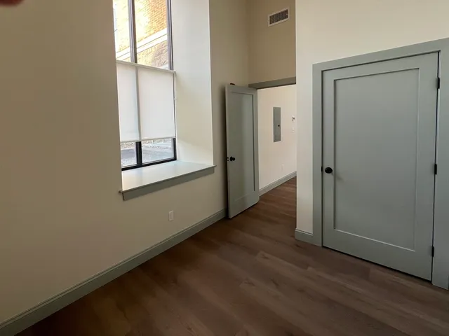 an empty room with wooden floor closet and windows