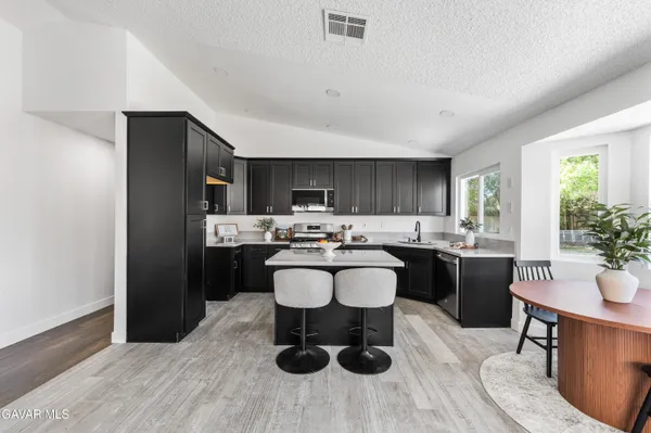 a living room with stainless steel appliances kitchen island granite countertop a sink dishwasher a dining table and chairs with wooden floor