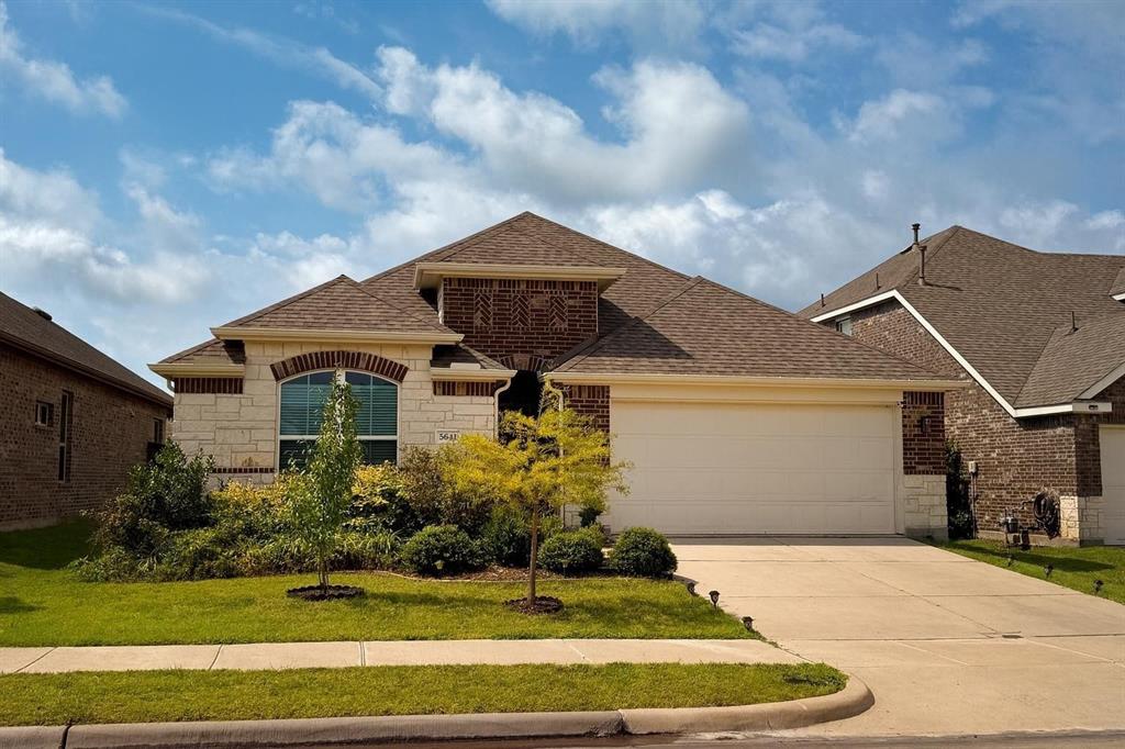 Brick and stone facade residence featuring an arched window, a two-car garage, and a concrete driveway