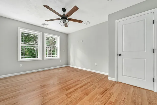 an empty room with wooden floor ceiling fan and windows