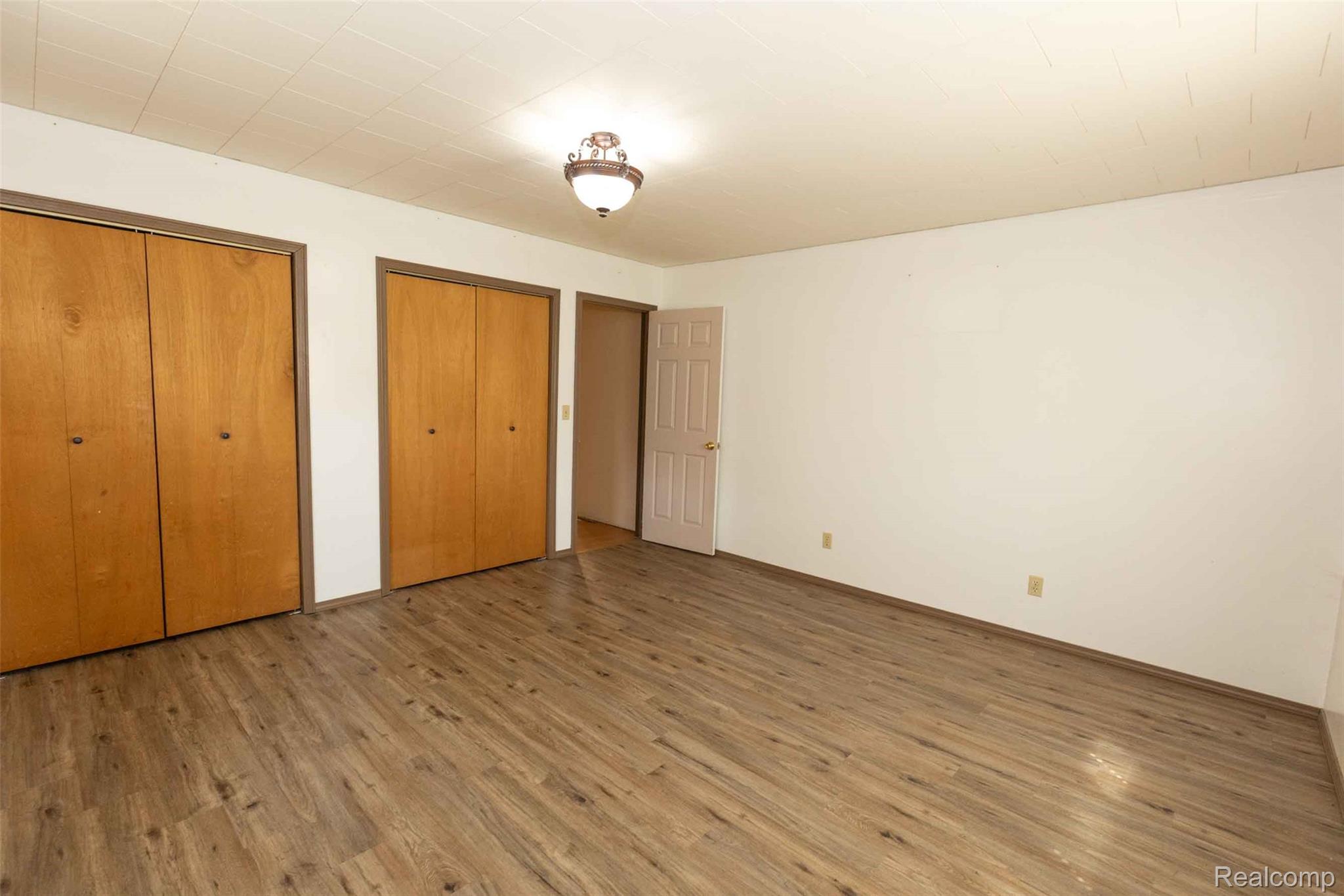 5761 Genesee Road Lapeer, MI 48446 - Photo 18 of 52 Spacious room featuring wood-finish flooring, two sets of bi-fold closet doors, a neutral wall color, and a ceiling-mounted light fixture