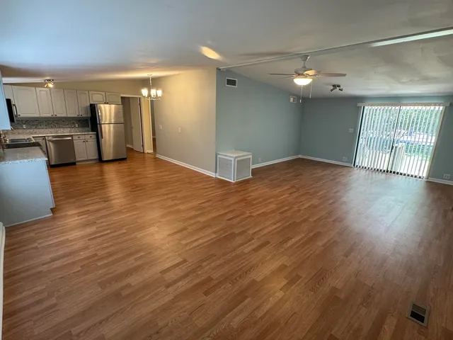 a view of empty room with wooden floor and kitchen view