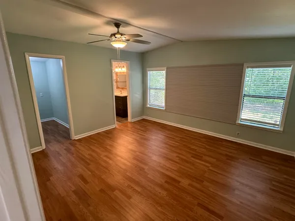 an empty room with wooden floor fan and windows